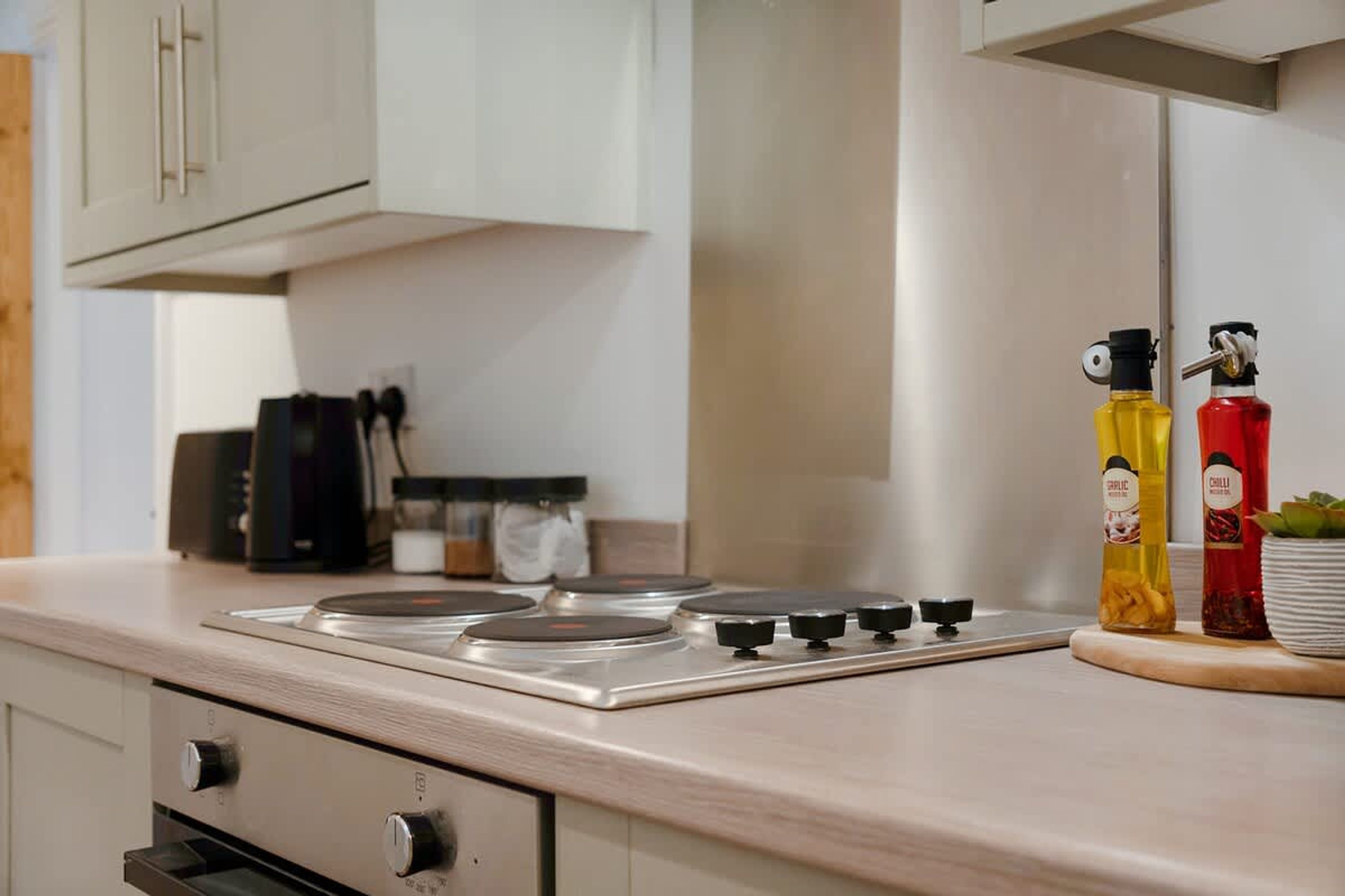 A kitchen with a gas stove, a range hood, and two condiment bottles.