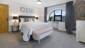 Quarto com cama, mesas de cabeceira, um banco, janela com cortinas e vista para o exterior.