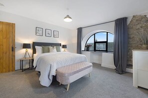 Ein Schlafzimmer mit einem Bett, Nachttischen, einer Bank, einem Fenster mit Vorhängen und Blick nach draußen.