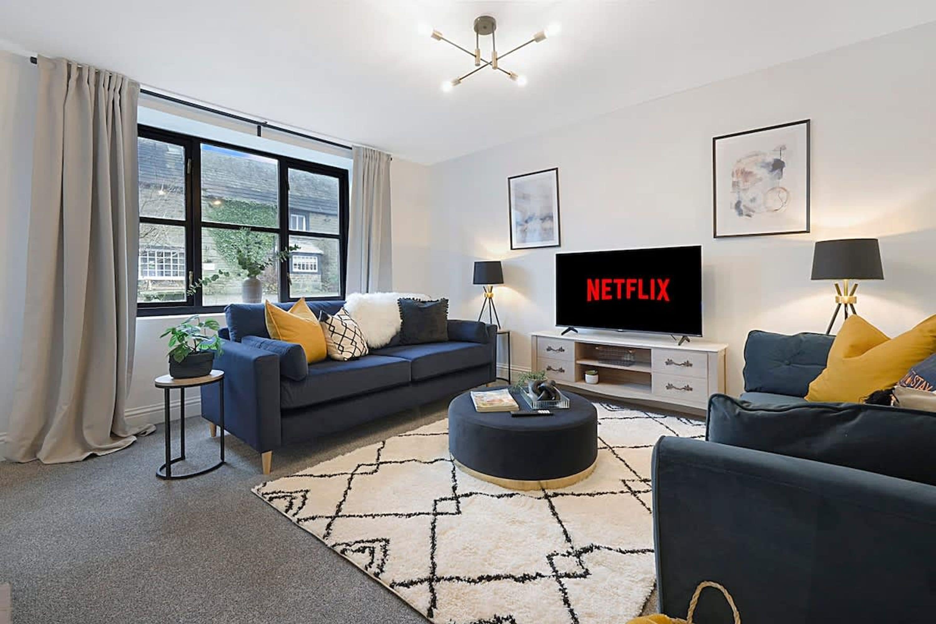 Una sala de estar moderna con un sofá, una mesa de centro y un televisor de pantalla plana mostrando 'NETFLIX'.