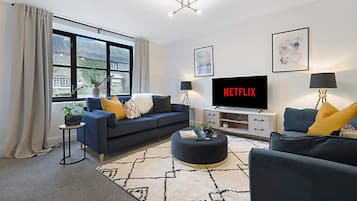 Una sala de estar moderna con un sofá, una mesa de centro y un televisor de pantalla plana mostrando 'NETFLIX'.