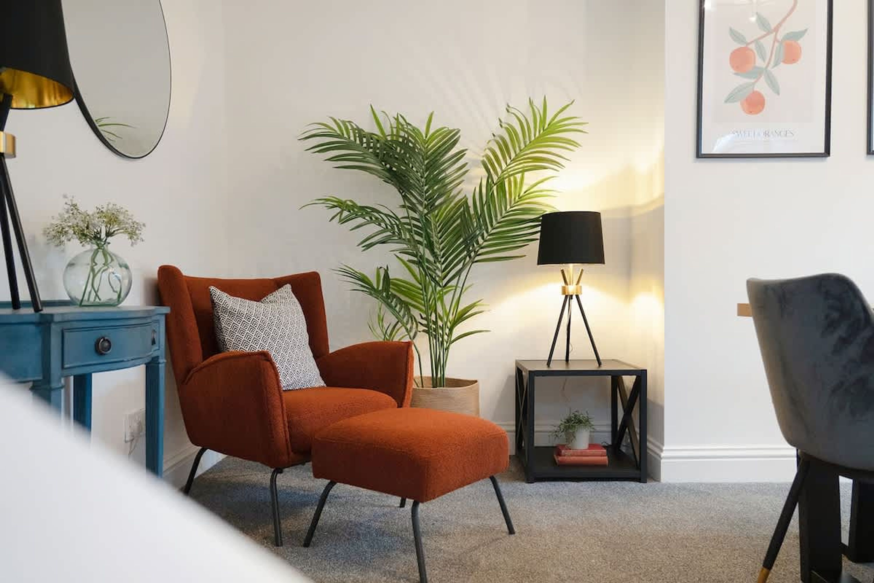 A room with a red armchair, a potted plant, a lamp, and a framed picture on the wall.