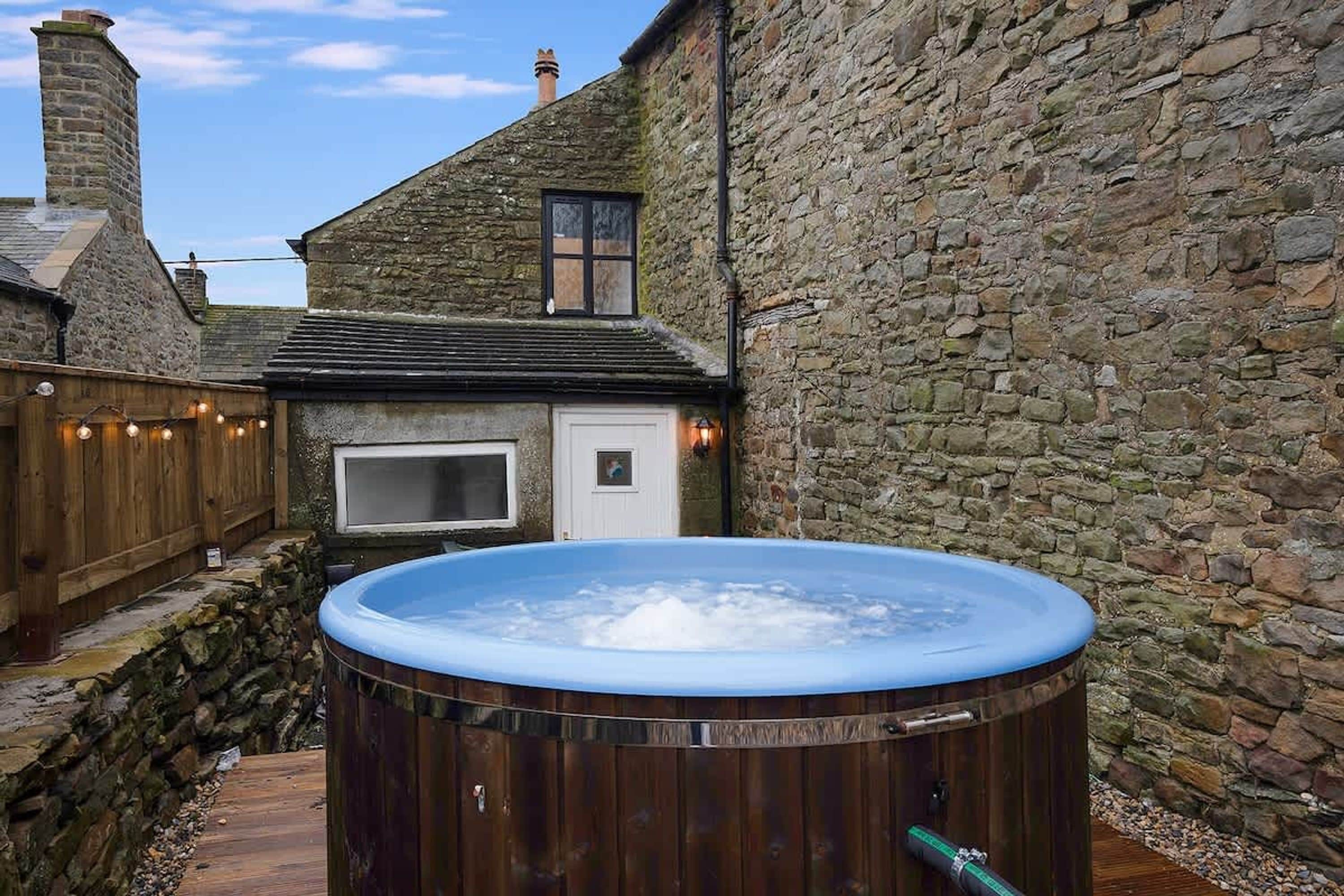 A hot tub in a stone-walled courtyard with a wooden deck and a small window.