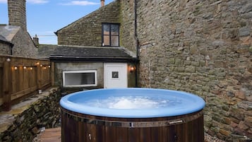 Un jacuzzi en un patio con paredes de piedra, una cubierta de madera y un ventanal.