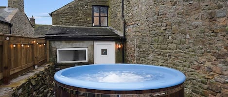 A hot tub in a stone-walled courtyard with a wooden deck and a small window.