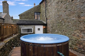A hot tub in a stone-walled courtyard with a wooden deck and a small window. - Detached Three Bedroom Family Home Hot Tub Stay (Barnard Castle)