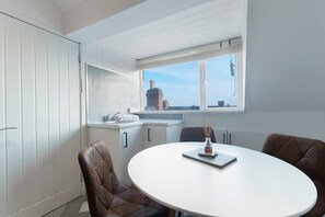 A modern kitchen with white cabinetry, a round dining table, and a view of a cityscape through a window. - Central Darlington Sleeps 8 With Wifi and Parking (Darlington)