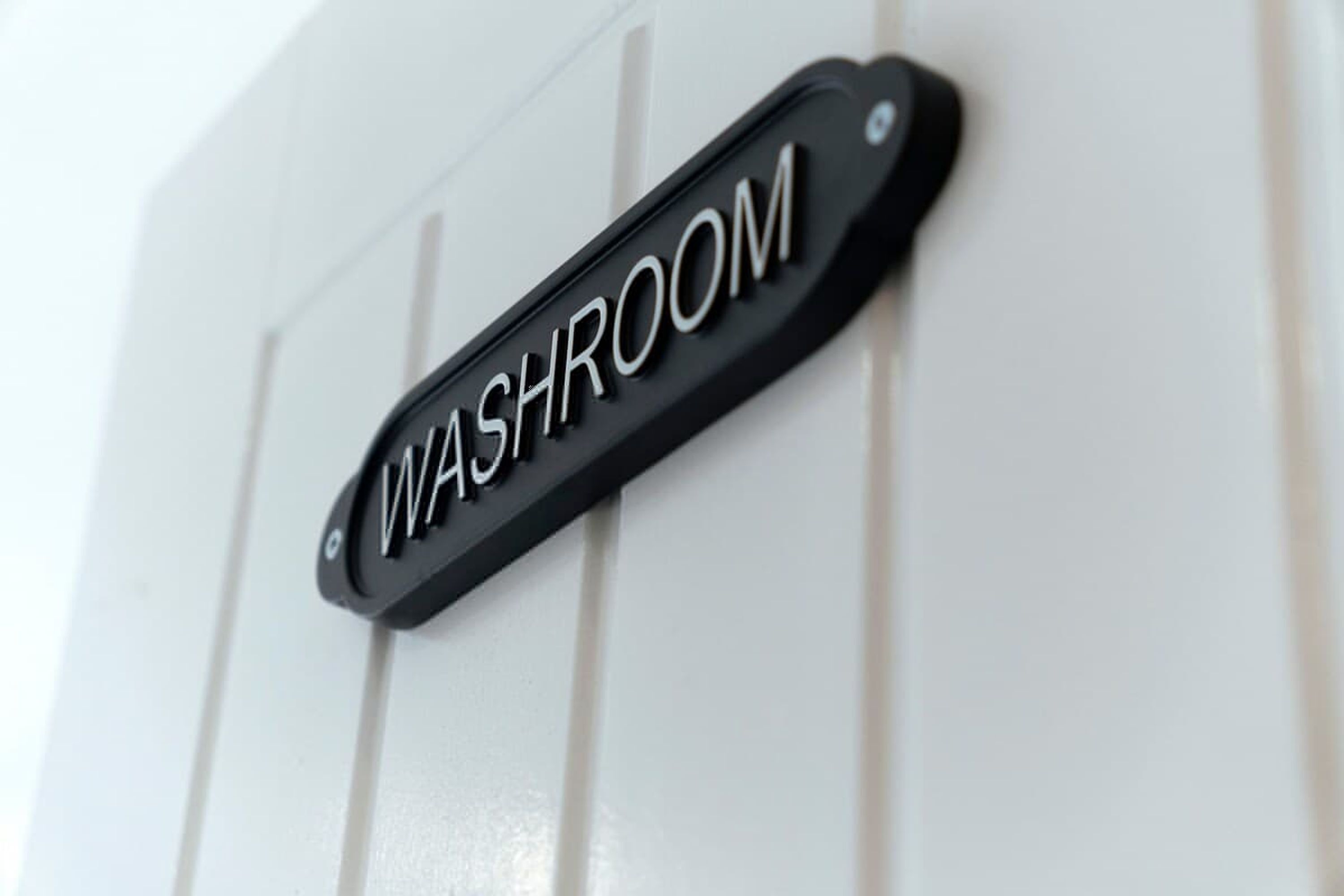 A black sign with white lettering that reads 'WASHROOM' mounted on a white door.