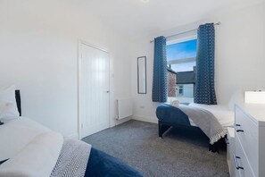 A bedroom with a bed, a bedside table, a dresser, a window with curtains, and a door. - Central Darlington Sleeps 8 With Wifi and Parking (Darlington)