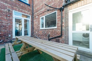 A wooden bench in a courtyard with a brick wall and a glass door. - Central Darlington Sleeps 8 With Wifi and Parking (Darlington)