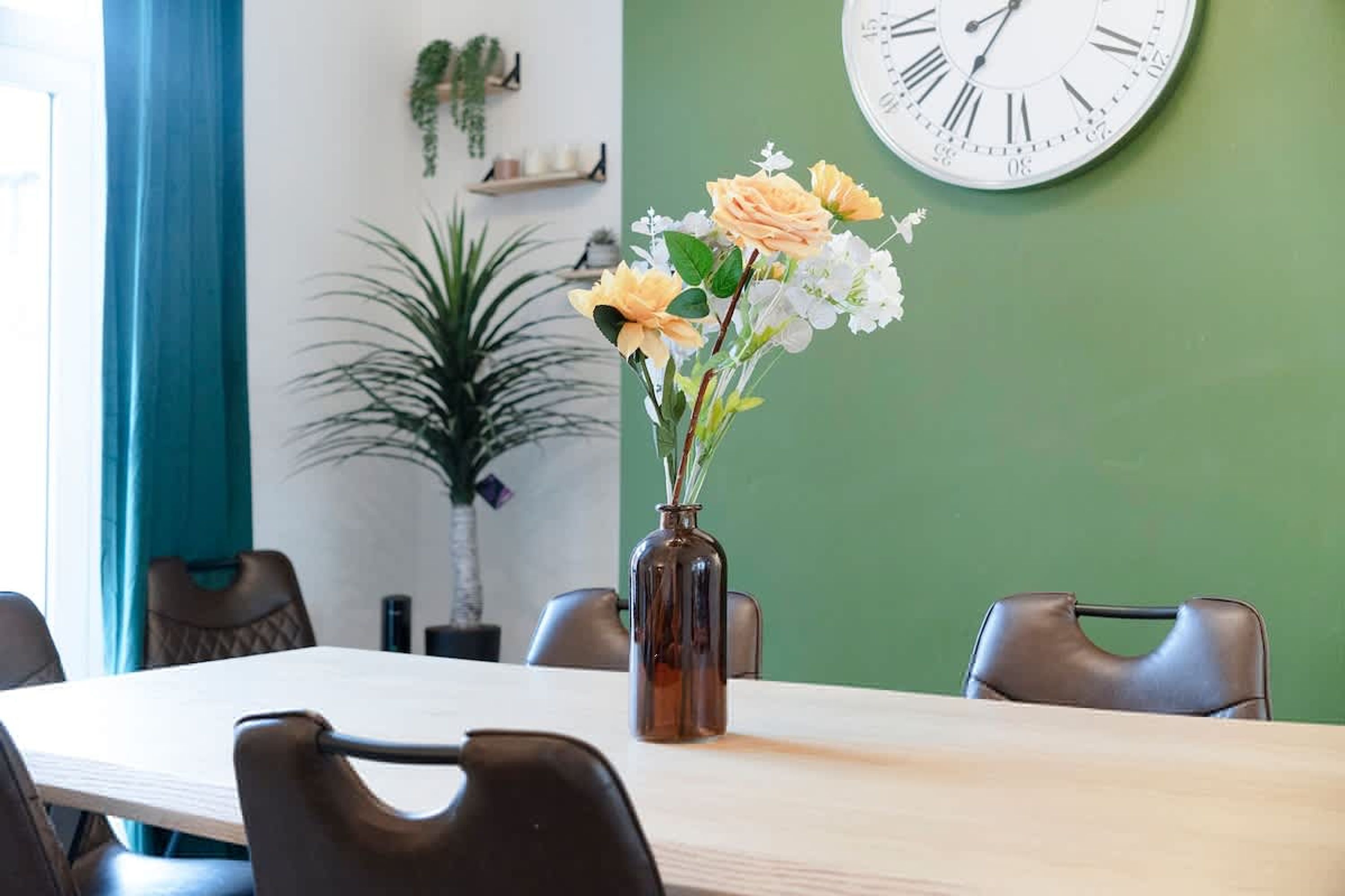 A conference room with a table, chairs, a clock, and a vase with flowers.
