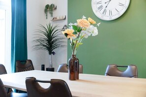 Uma sala de conferência com uma mesa, cadeiras, um relógio e um vaso com flores.