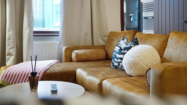 A modern living room with a brown leather sofa, a round coffee table, and a window with curtains. - Bright 4BR Norton Getaway Sleeps 7 by Stay With Us (Stockton-on-Tees)