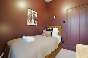 A bedroom with a bed, a headboard, a wall-mounted artwork, a door, and a towel on the bed. - Bright 4BR Norton Getaway Sleeps 7 by Stay With Us (Stockton-on-Tees)