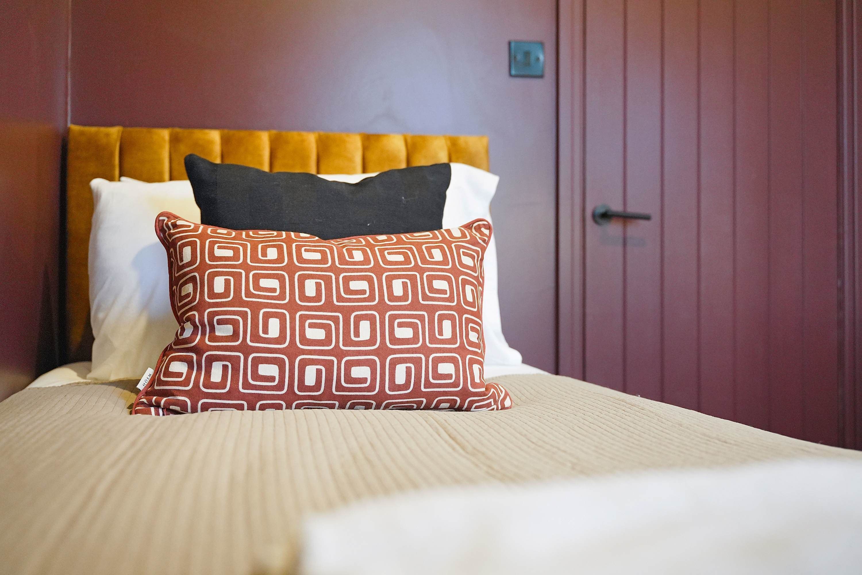 A hotel room with a bed, a headboard, and a door.