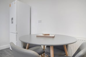 Ein Zimmer mit einem runden Tisch, zwei Stühlen, einem weißen Kühlschrank und einer Heizung.
