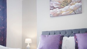 A hotel room with a bed, a nightstand, a lamp, and a floral painting on the wall. - Spacious Retreat With Backyard Bliss Sleeps 7 (Bishop Auckland)