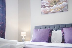 Ein Hotelzimmer mit einem Bett, einem Nachttisch, einer Lampe und einem floralen Gemälde an der Wand.