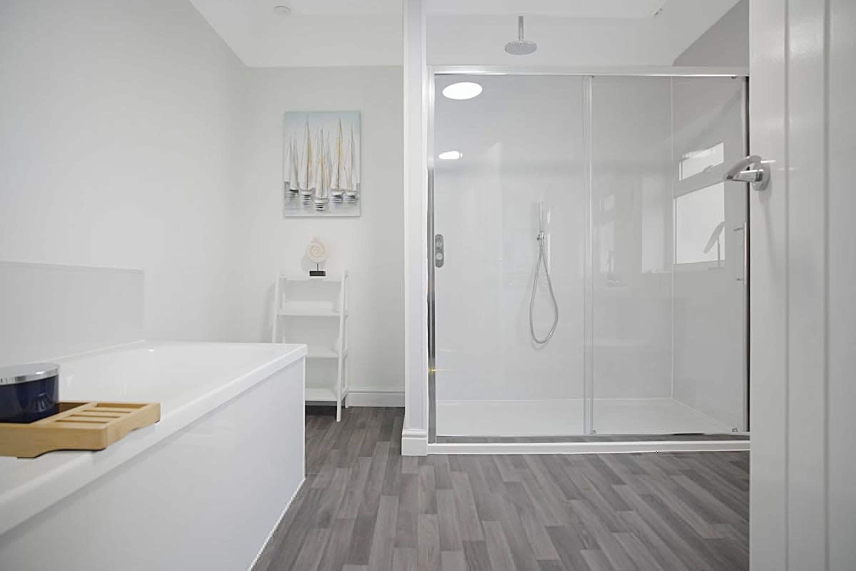 Une salle de bain moderne avec une douche à l’italienne en verre, une baignoire blanche et une étagère en bois.