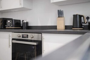 Une cuisine équipée d’un four encastré, d’une machine à café et d’un bloc à couteaux posé sur le plan de travail.