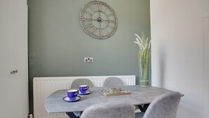 A dining area with a round table, two chairs, a clock on the wall, and a vase with long white flowers. - Central Darlington Sleeps 5 For Work or Leisure (Darlington)