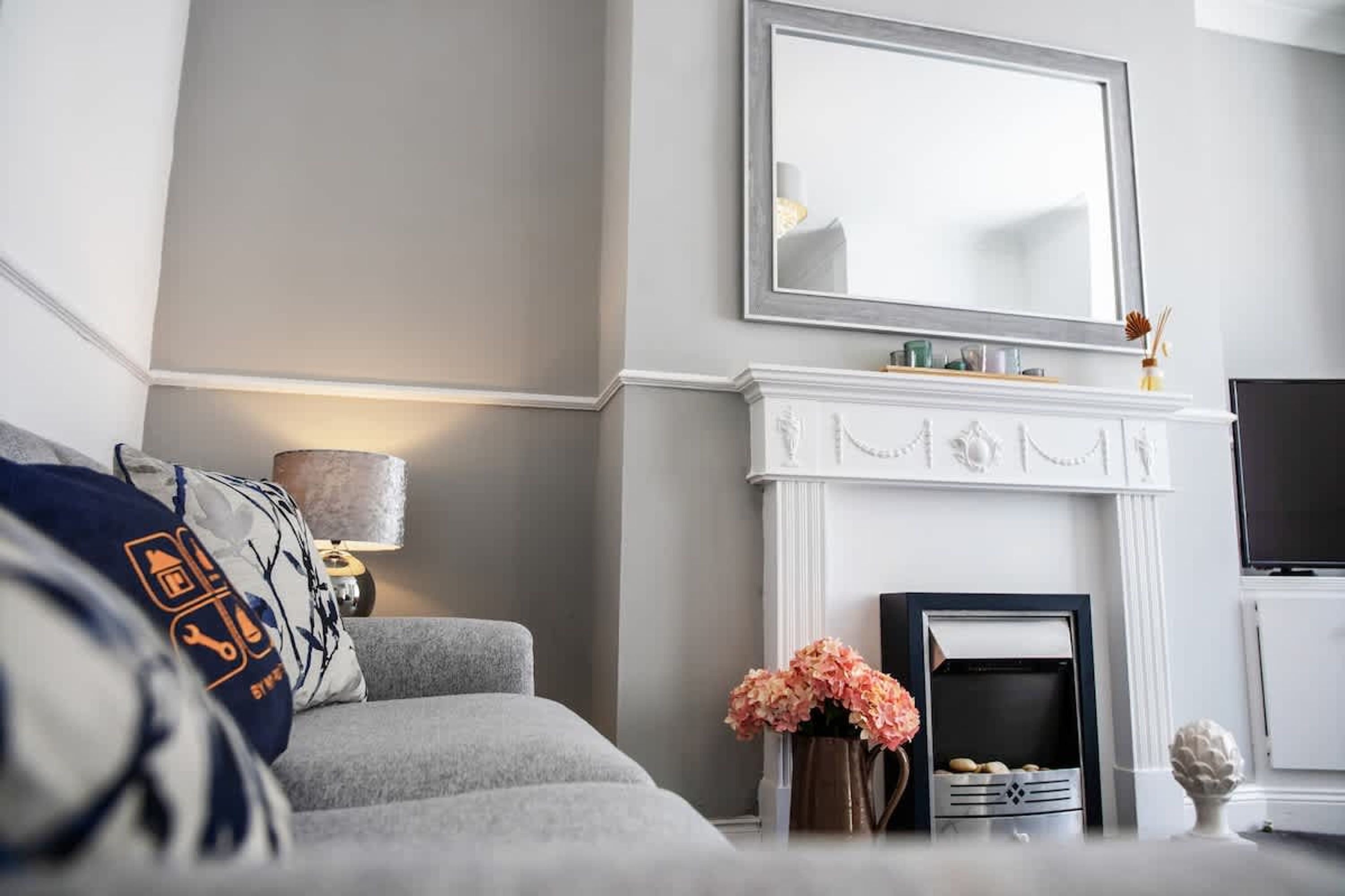 Un salon avec un canapé gris, une cheminée, un téléviseur et un miroir au mur.