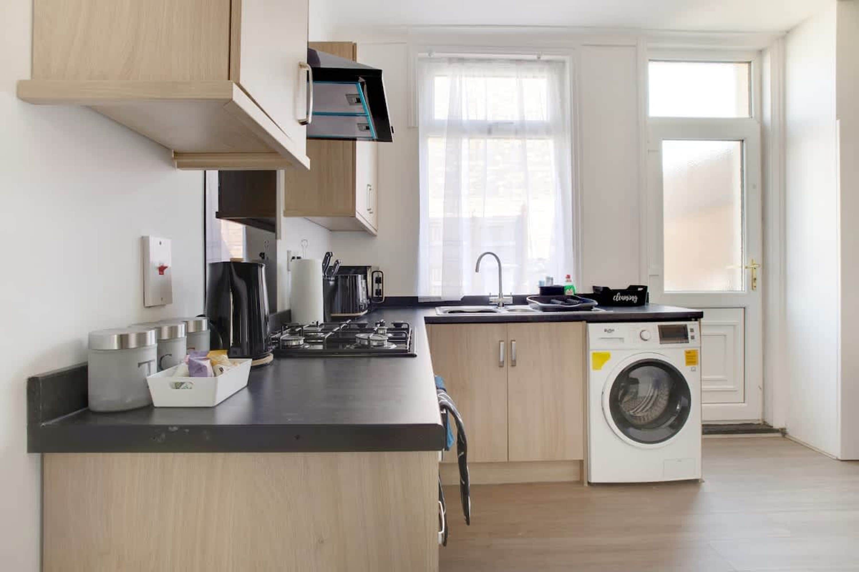 Une cuisine moderne dotée d’un lave-linge encastré, de meubles en bois et d’une fenêtre laissant entrer la lumière naturelle.