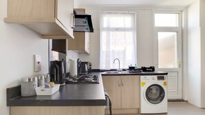 A modern kitchen with a built-in washing machine, wooden cabinets, and a window providing natural light. - Central Darlington Sleeps 5 For Work or Leisure (Darlington)