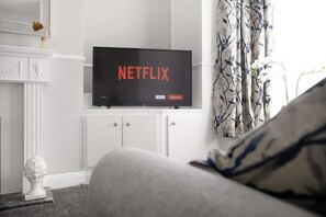 Ein Fernseher zeigt das Netflix-Logo und steht in einem Schrank in einem Raum mit weißem Kamin und Vorhängen.