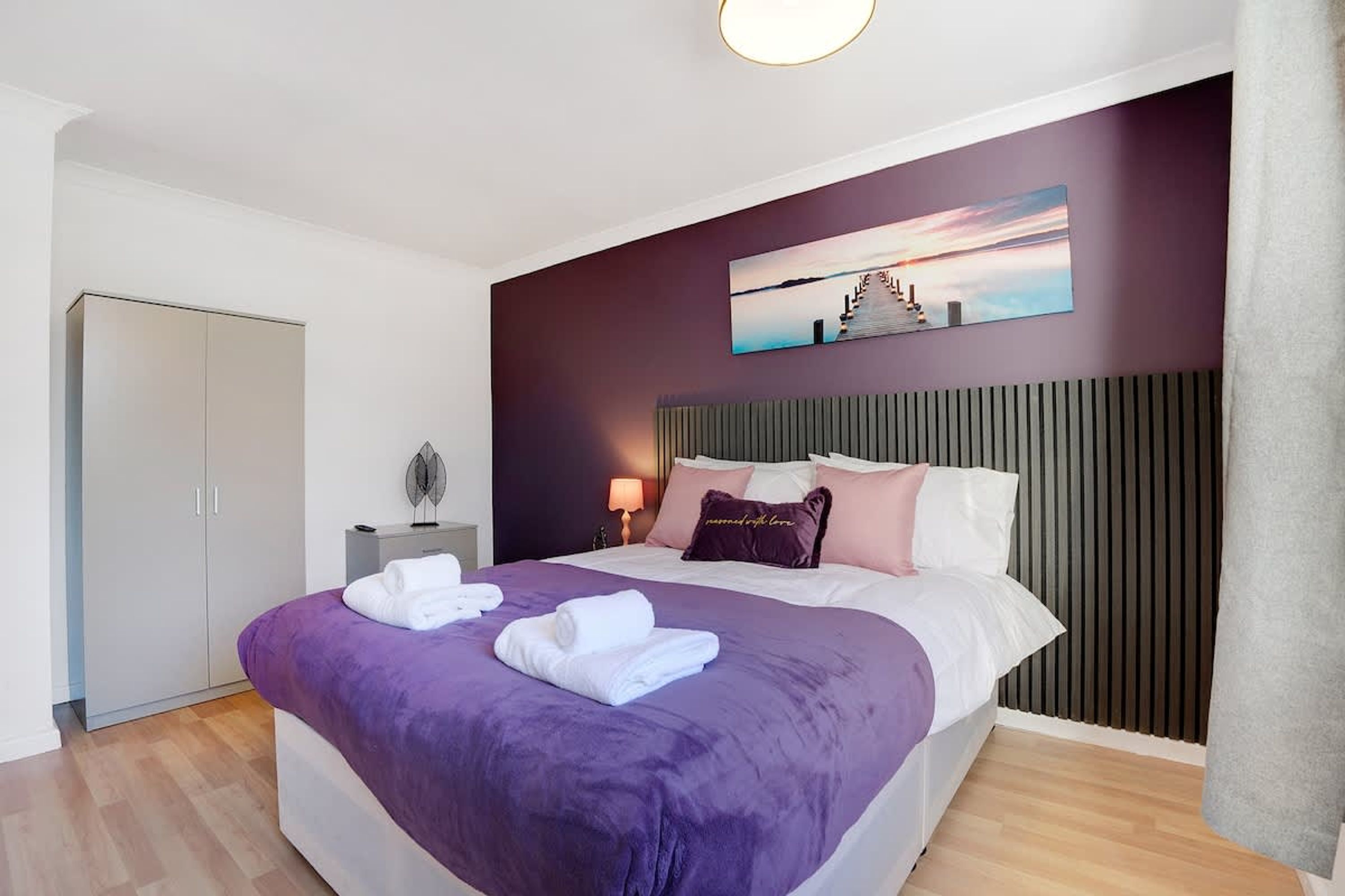 Una habitación de hotel con cama, mesita de noche, lámpara y un cuadro en la pared.