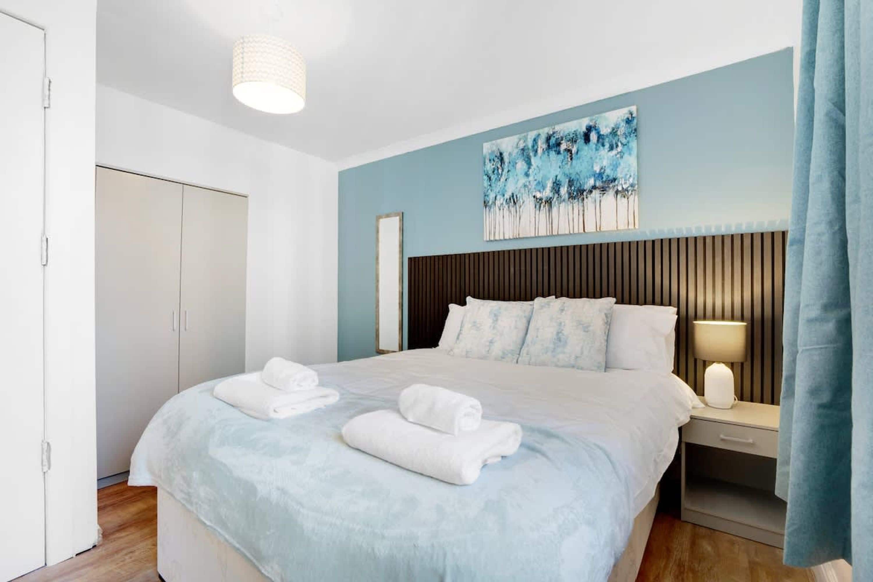 Une chambre d’hôtel avec un lit, une table de chevet, une lampe, un tableau au mur et une armoire.