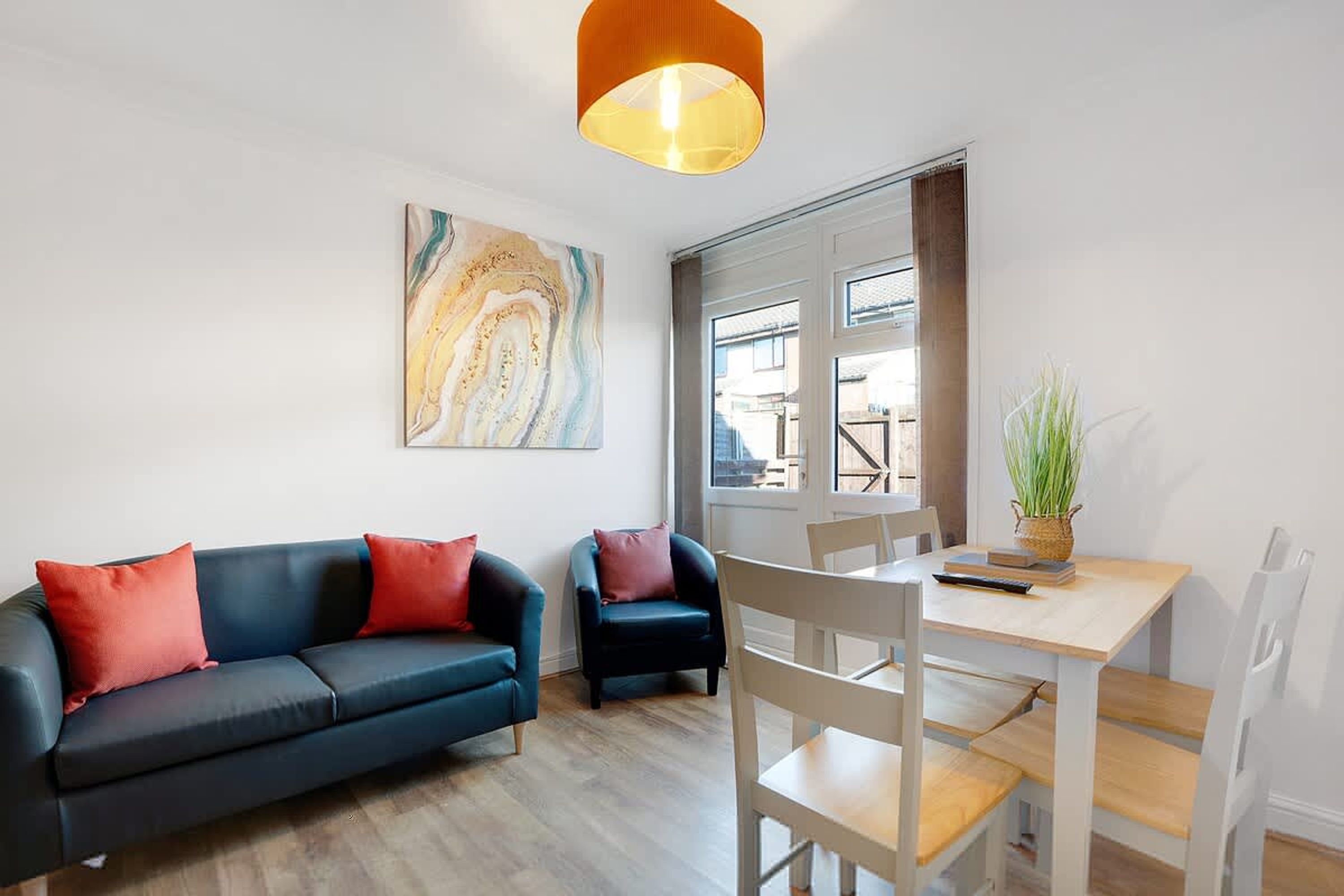 Una sala de estar moderna con un sofá azul, una mesa de comedor blanca y un cuadro abstracto grande en la pared.