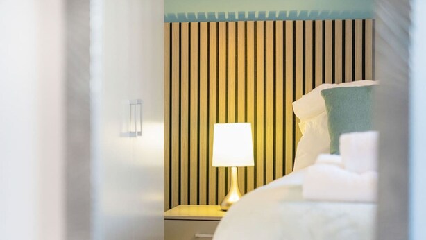 A hotel room with a bed, a bedside table with a lamp, and a vertical striped wall. - 4BR in Stafford Place Sleeps 7 Wifi Free Parking (Peterlee)