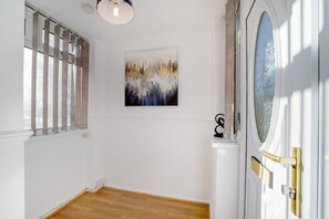 Ein Flur mit Holzboden, einer weißen Tür mit Glasfenster und einem Gemälde an der Wand.
