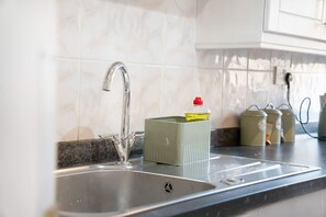 Eine Küche mit einer Edelstahlspüle, einer Marmor-Spritzschutzwand und einem grünen Behälter auf der Arbeitsfläche.