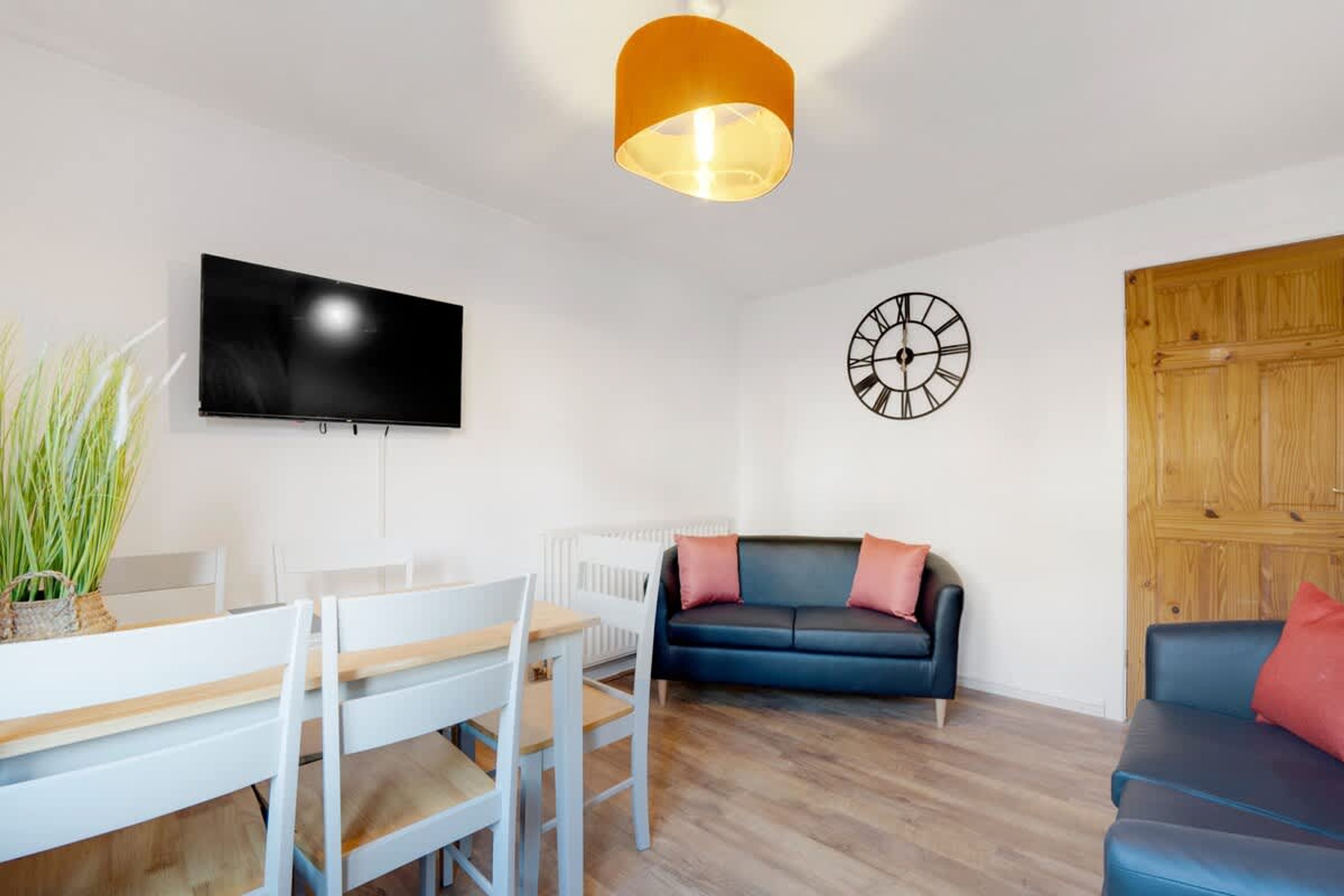 A modern living room with a flat-screen TV, a clock, a sofa, and a dining area with chairs.