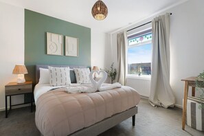 Ein Schlafzimmer mit einem Bett, Nachttischen, einer Lampe, einem Fenster mit Vorhängen und Wandbildern.