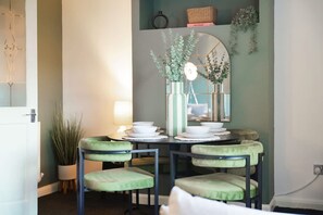 A dining area with a table set for four, a mirror above the table, and a potted plant to the left. - Charming 3 Bedroom Home Near Coast Town (Redcar)