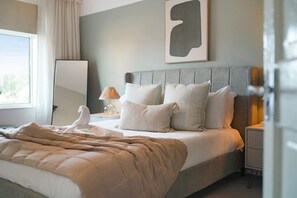 Ein ordentlich bezogenes Bett mit Daunendecke, einer Nachttischlampe und einem an der Wand befestigten abstrakten Kunstwerk.