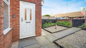 A residential property with a white door, brick walls, a small garden with gravel and plants, and a black fence. - Charming 3 Bedroom Home Near Coast Town (Redcar)