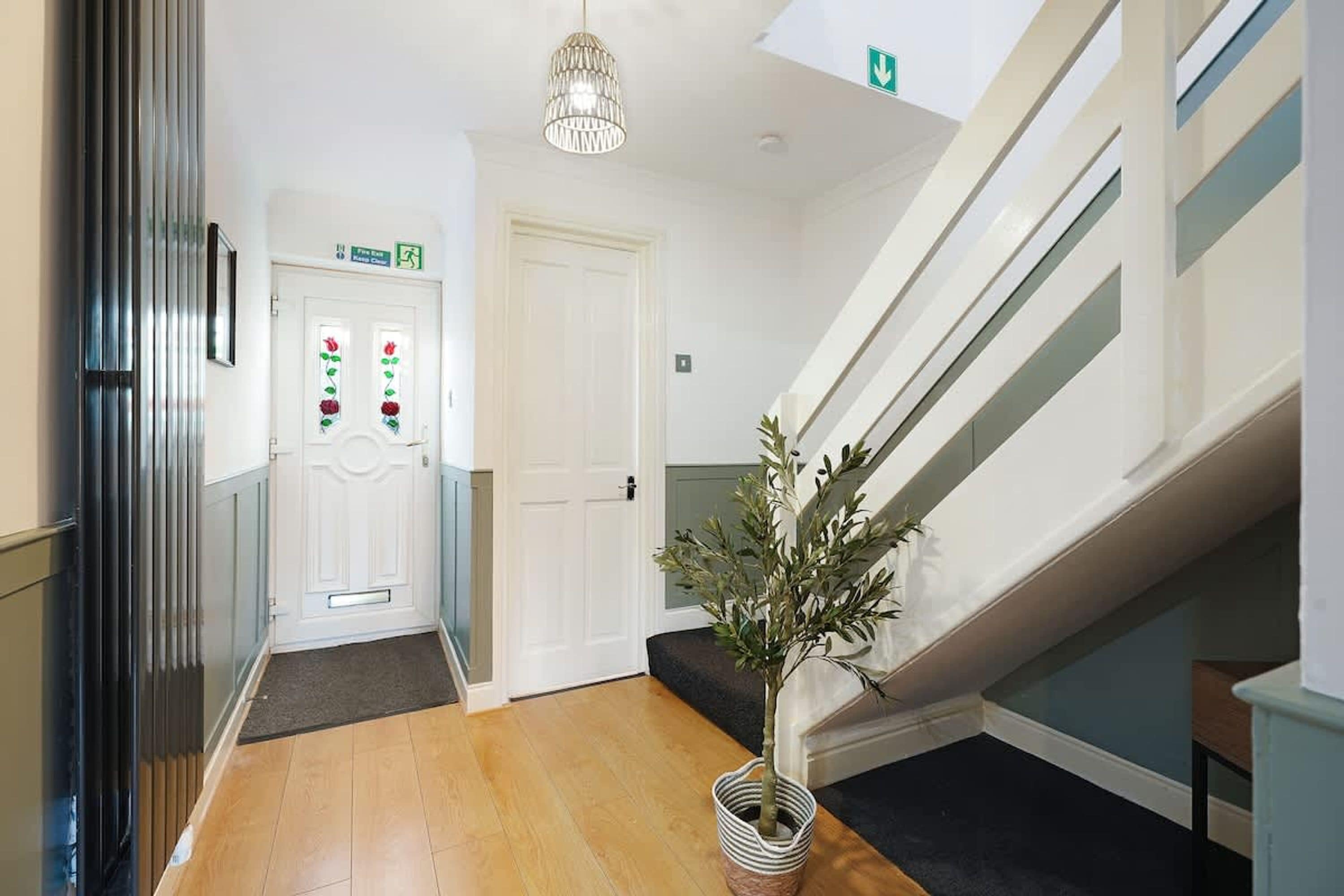 A hallway with a wooden floor, a staircase, a potted plant, and a door with a flower design.