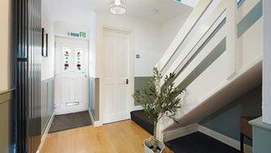 A hallway with a wooden floor, a staircase, a potted plant, and a door with a flower design. - Charming 3 Bedroom Home Near Coast Town (Redcar)