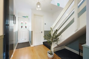 A hallway with a wooden floor, a staircase, a potted plant, and a door with a flower design. - Charming 3 Bedroom Home Near Coast Town (Redcar)
