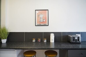 Une cuisine avec une affiche encadrée, deux tabourets, un grille-pain et des bocaux posés sur le comptoir.