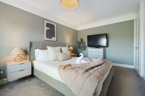 Une chambre à coucher comprenant un lit, une table de chevet, une lampe, un téléviseur et une œuvre d’art accrochée au mur.