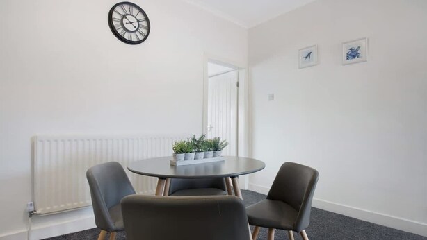 Une pièce avec une table ronde, deux chaises, une horloge au mur et un radiateur.