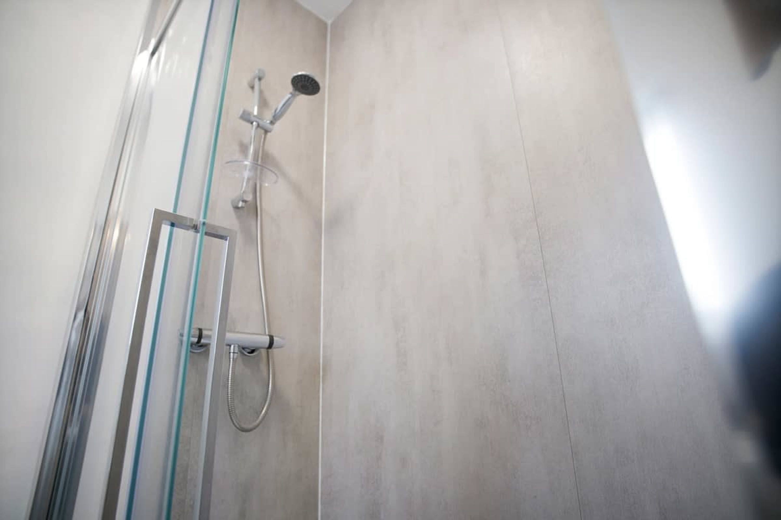 A shower with a glass door, a handheld showerhead, and a wall-mounted faucet.
