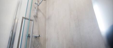 A shower with a glass door, a handheld showerhead, and a wall-mounted faucet.