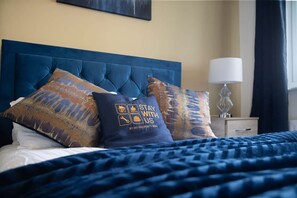 Quarto de hotel com uma cama grande, roupa de cama azul e almofadas decorativas.