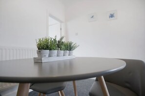 Ein runder Tisch mit grauer Tischplatte und Holzbeinen, umgeben von grauen Stühlen. Auf dem Tisch stehen Blumentöpfe.